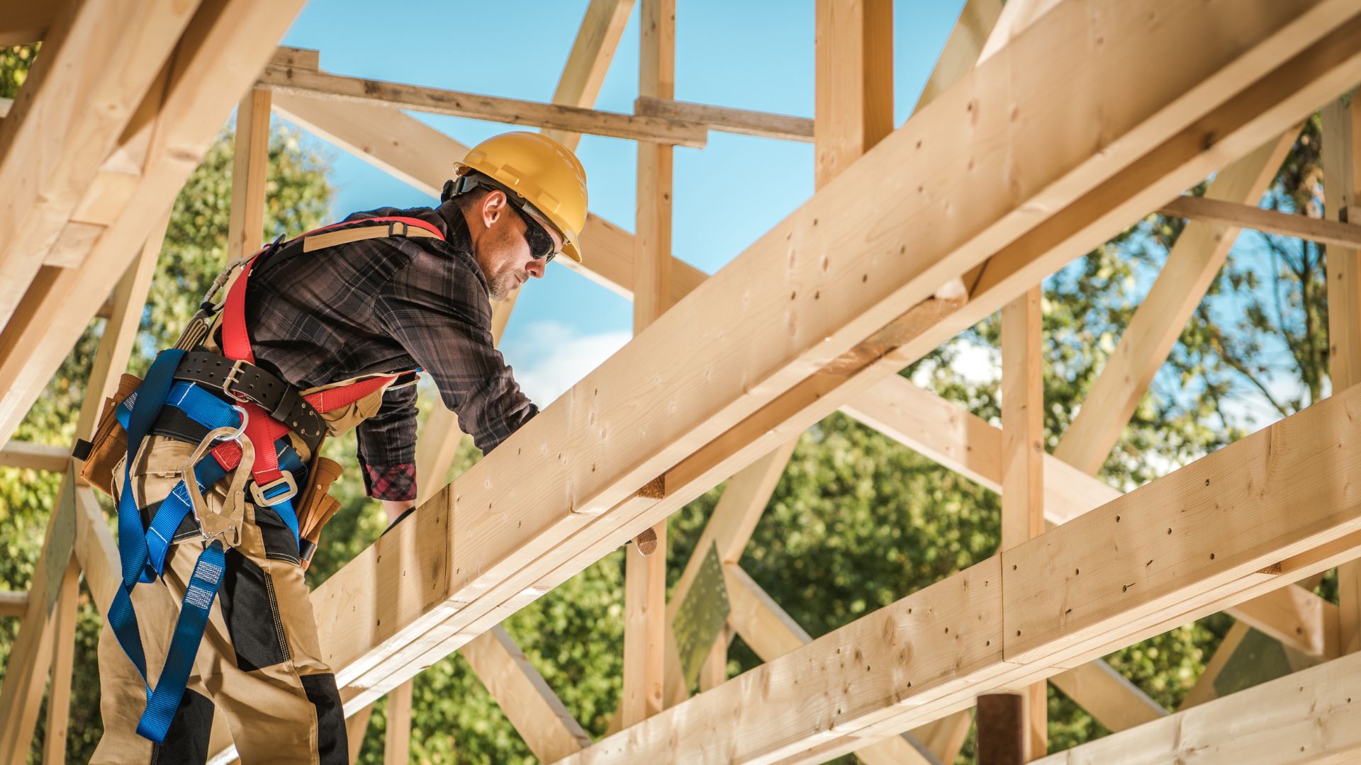 Construction worker in safety gear installing wooden roof framing
