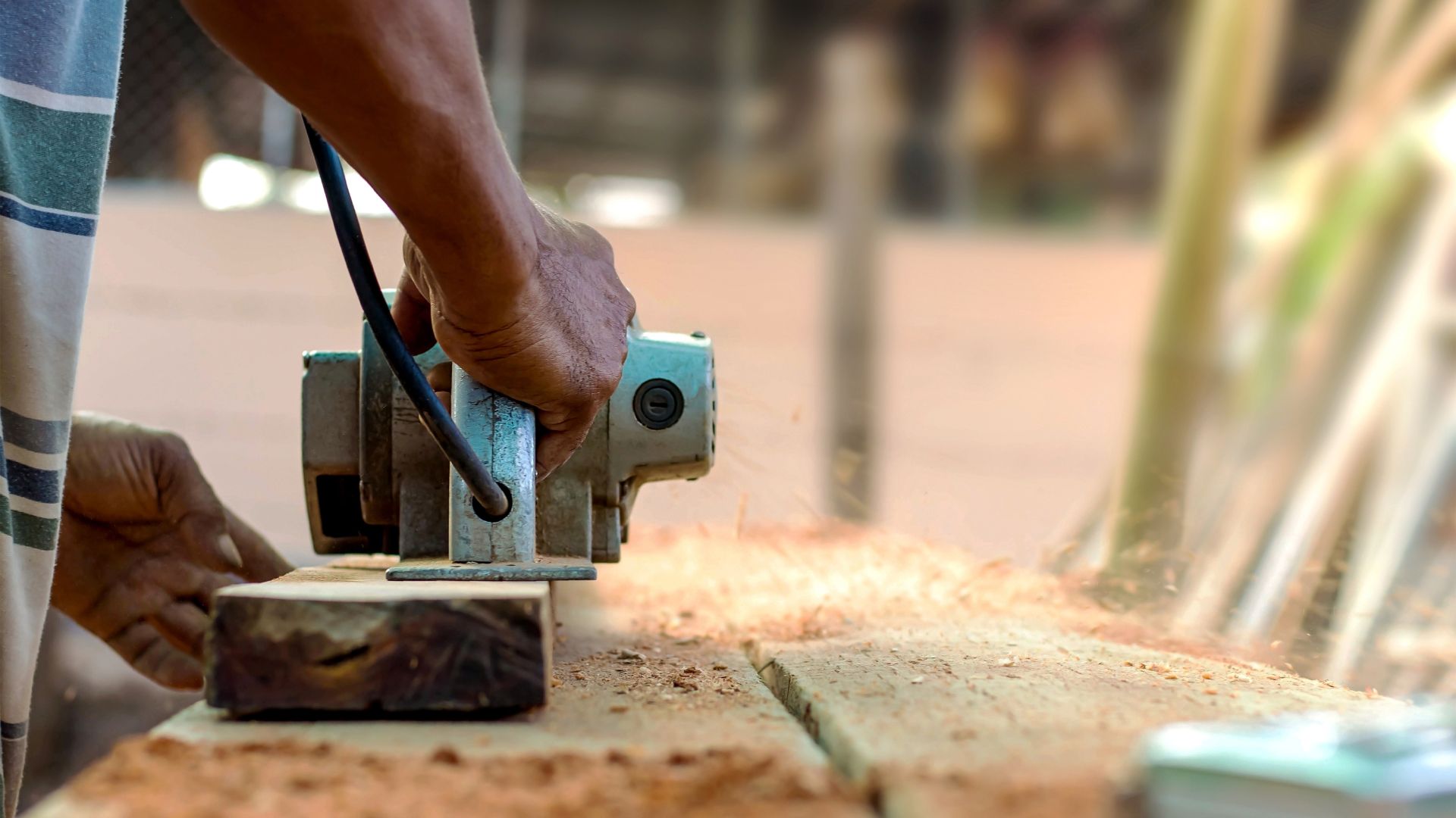 Woodworker using electric planer to smooth wooden board in workshop