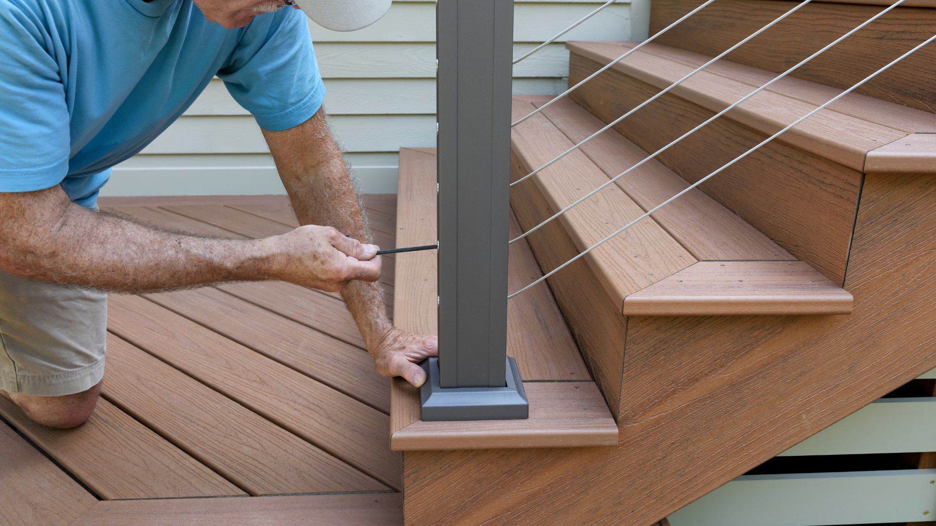 Worker installing wooden deck stairs with metal railing post