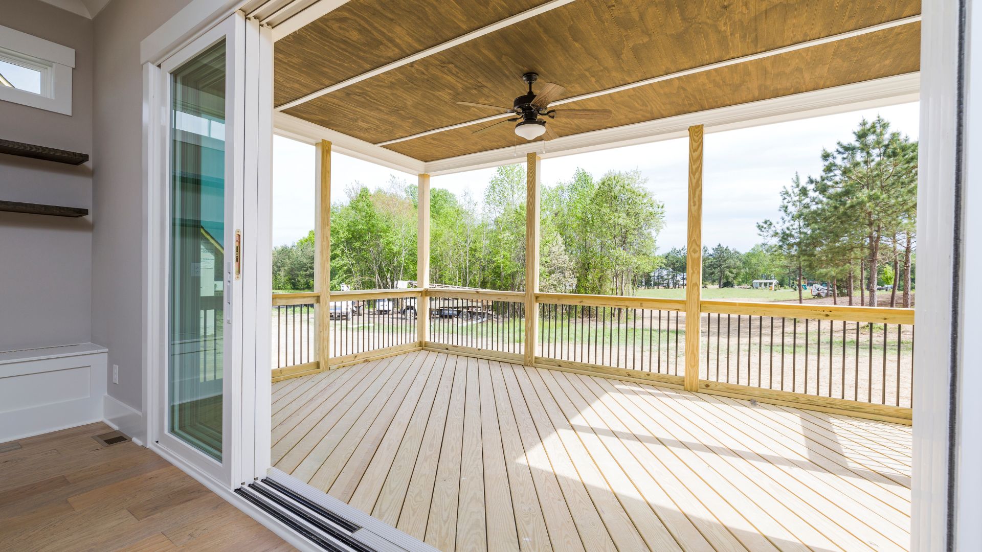 Spacious wooden deck with ceiling fan, overlooking green trees and landscape