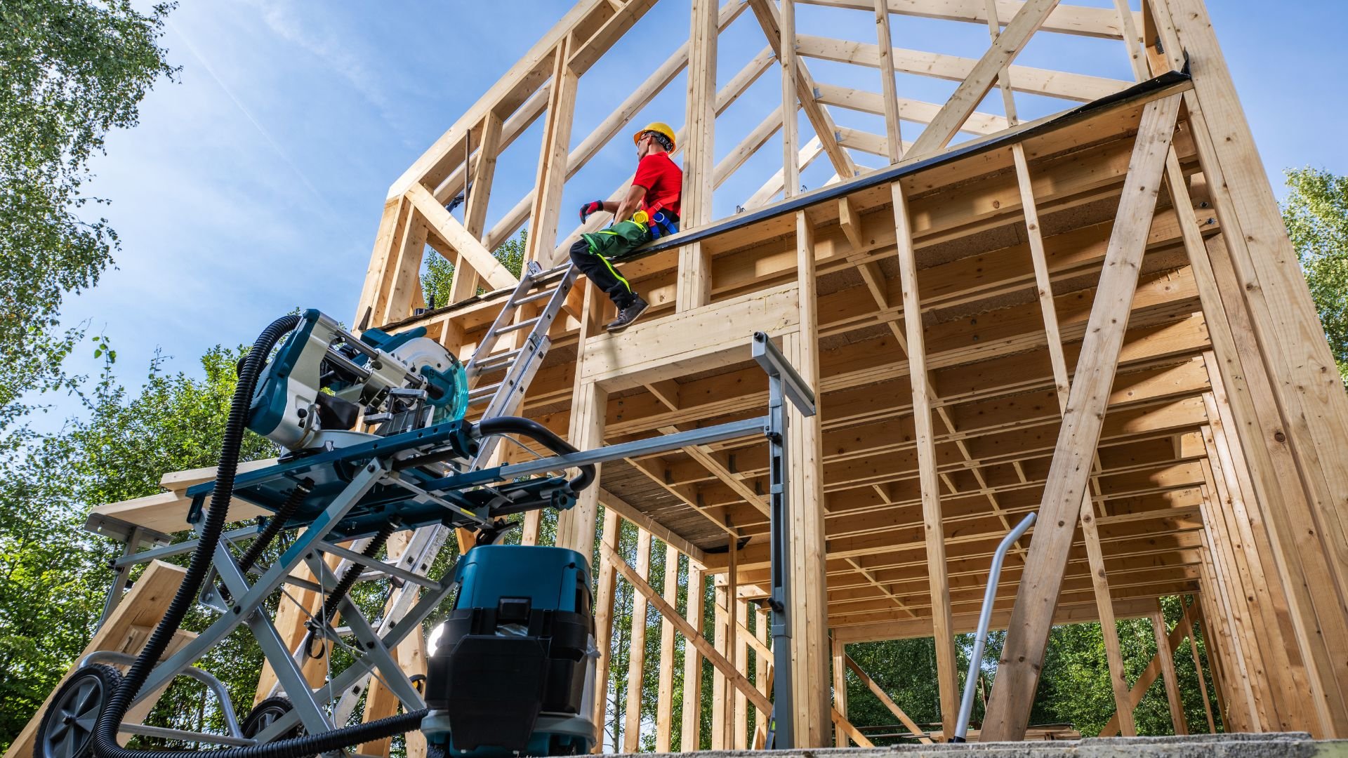 Construction worker on ladder building wooden frame structure with power tools